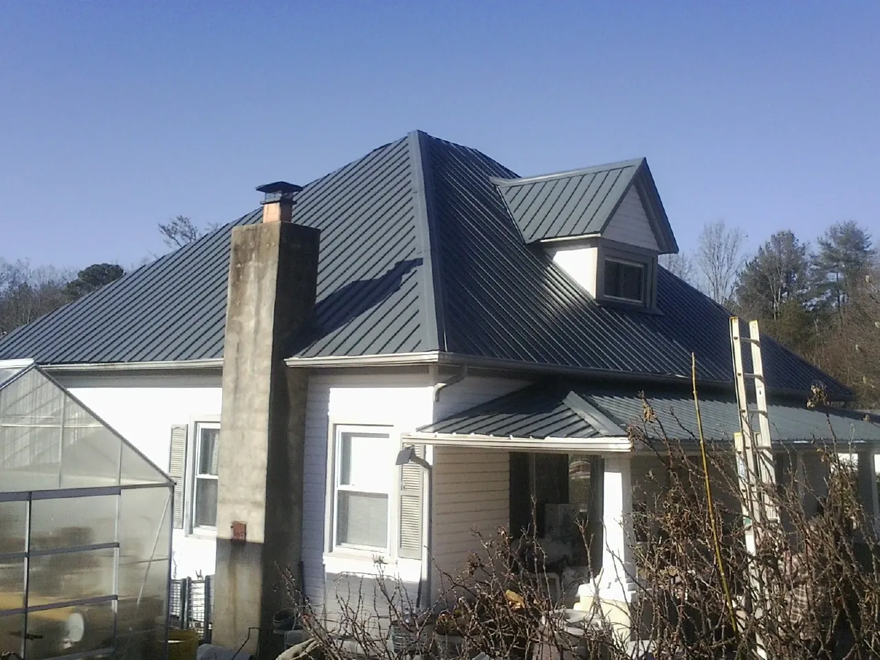 Dark blue standing seam metal roof on a white farmhouse with dormer — Slate & Tile Roof Repair by Roofing Brothers in Wyatt