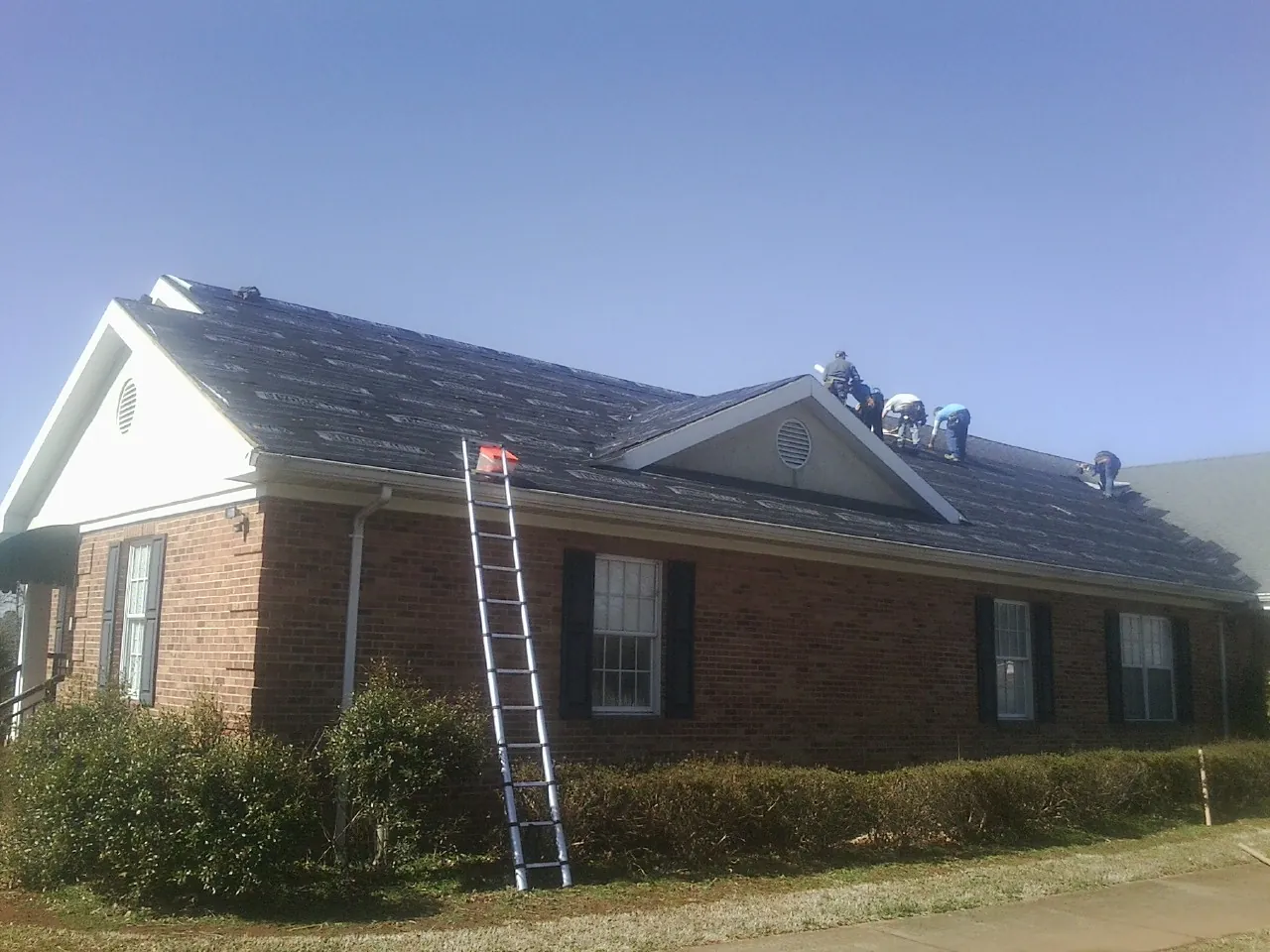 Crew tearing shingles off a brick ranch roof with a ladder set — Emergency Roof Repair work by our crew in Wyatt