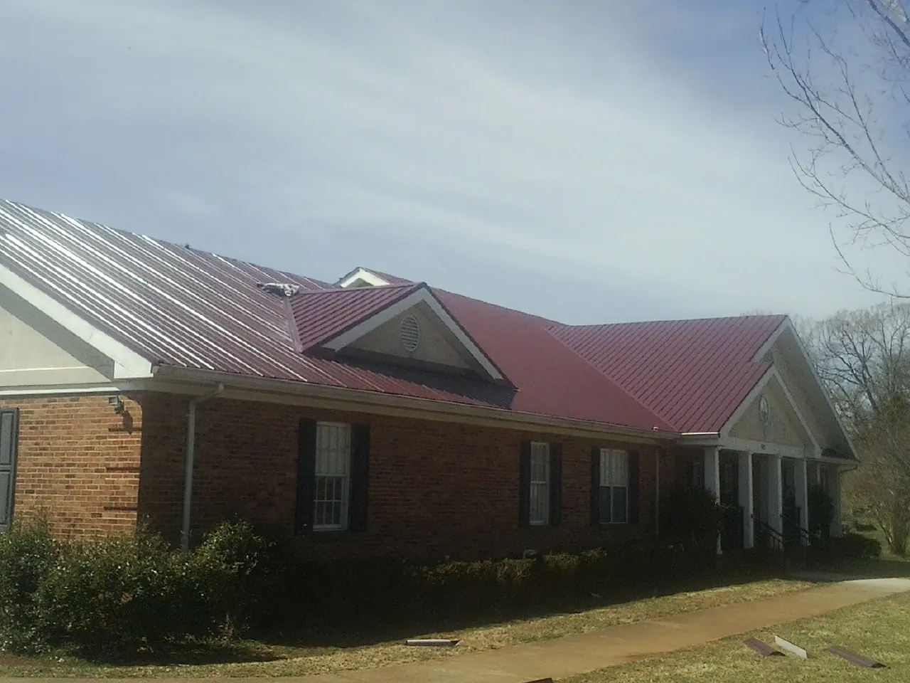 Red metal roof with gabled entries on a long brick building, from a Hail Damage Roof Repair job in Wyatt