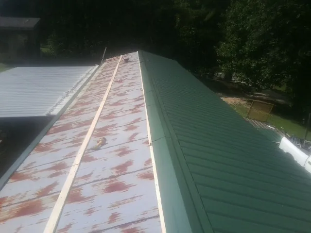 Old rusted panels beside newly installed green metal roofing — Wind Damage Roof Repair by Roofing Brothers in Wyatt