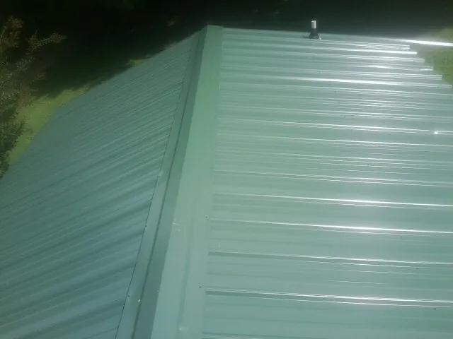 New green metal panels meeting at the ridge of a roof — Flat Roof Repair work by our crew in Wyatt