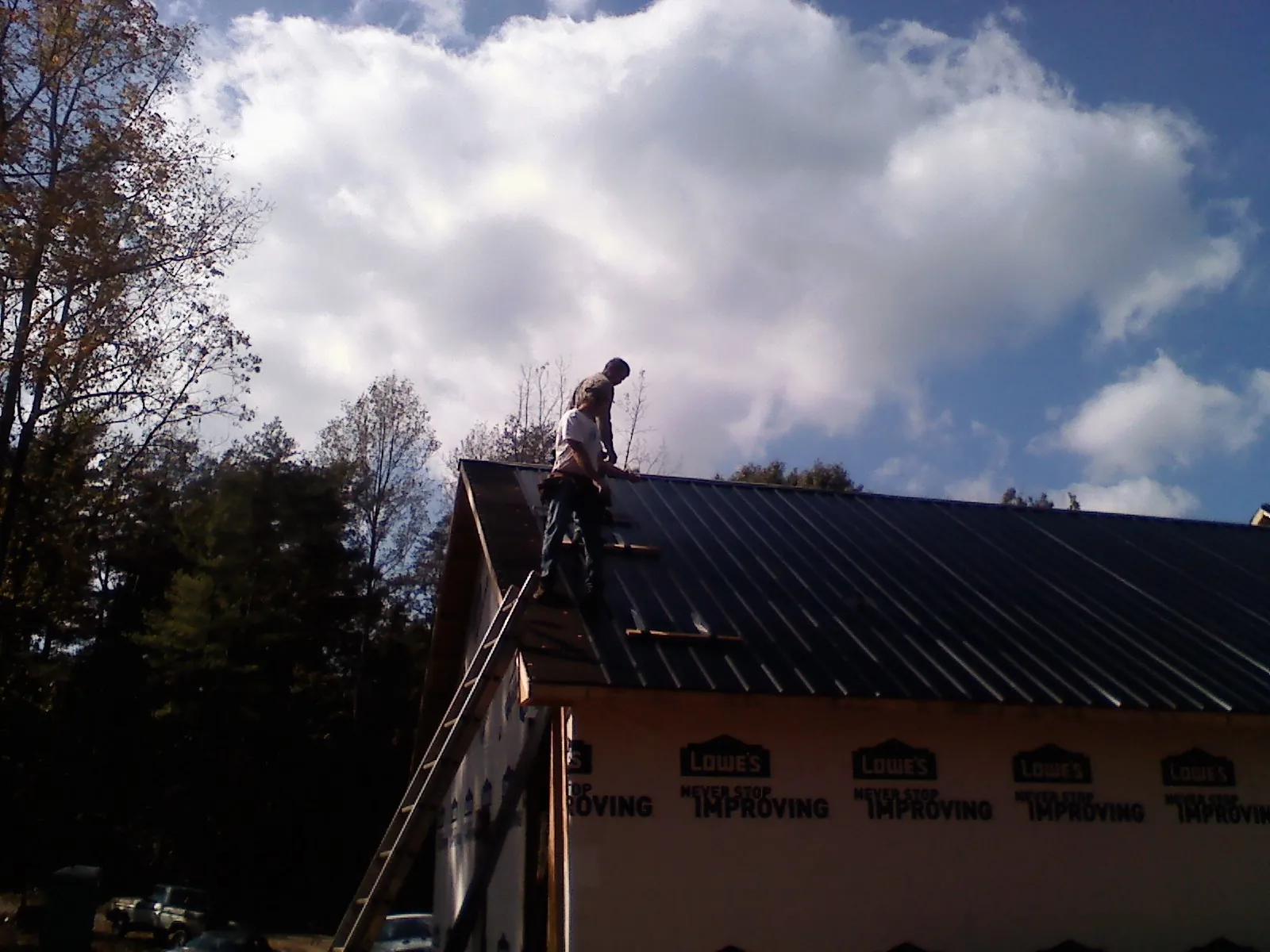 Roofer fastening dark metal panels high against a cloudy sky, from a Roof Inspection job in Wyatt